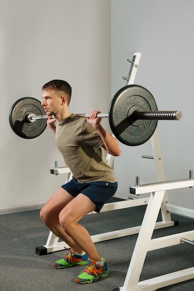 Athletic man doing squats exercise with dumbbell.