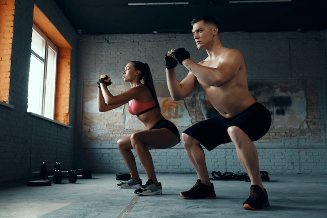 Confident fit couple standing in squatting position while exercising in gym together