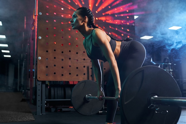 Fitnesswoman doing deadlift using barbell in gym.