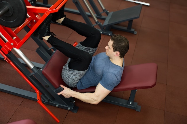 Attractive Young Man Doing Leg Press On Machine In Gym.