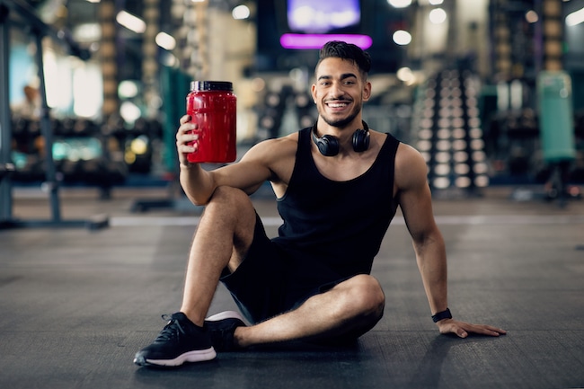 Arab Athlete Posing At Gym With Container Of Protein Whey In Hand