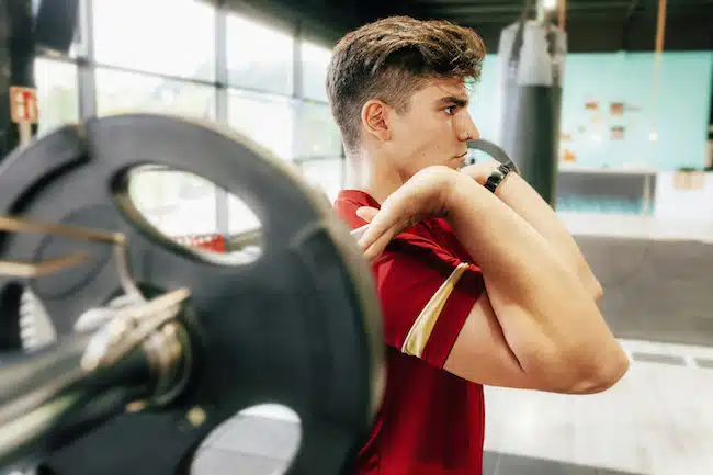 Sporty man in sportswear doing front squats with a barbell on the chest