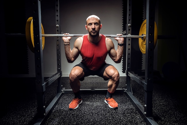 Strong muscular bodybuilder athletic man pumping up muscles with barbell on dark studio with power squat