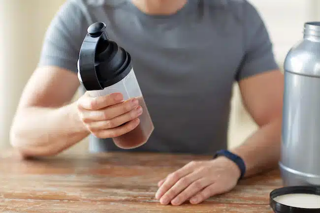 close up of man with protein shake bottle and jar creatine