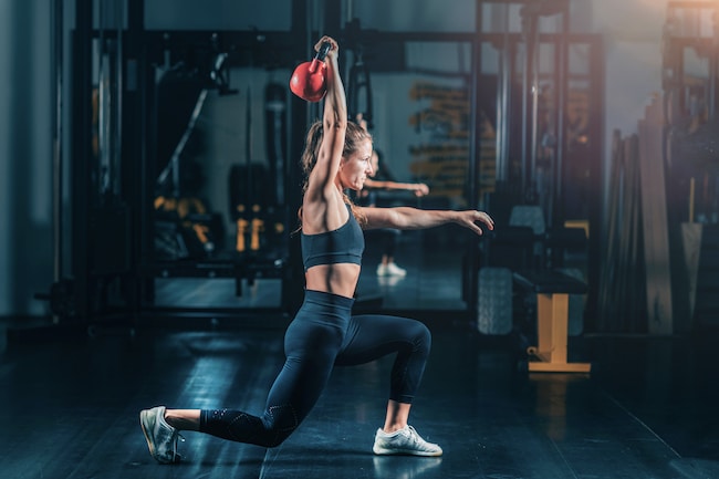 Woman Making Lunges with Kettlebell Over the Head.