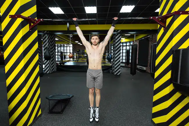 Muscular shirtless man doing pulling up on horizontal bar
