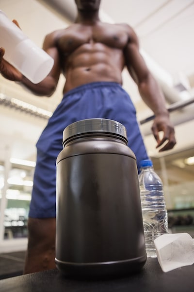Shirtless body builder scooping up protein powder in gym