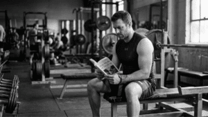 A weightlifter reading a book in the gym.