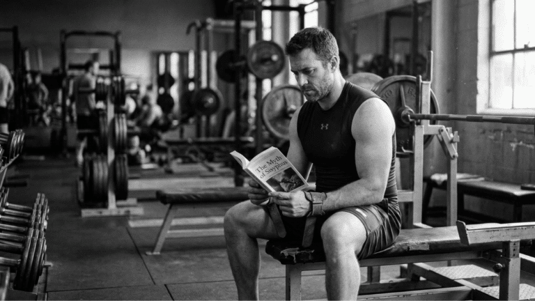 A weightlifter reading a book in the gym.