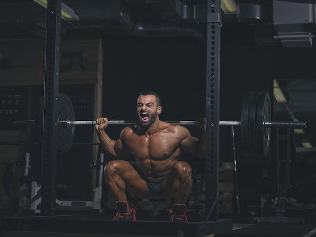 Bodybuilder performing squats with a barbell in gym