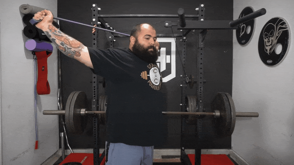 A strength coach shows how to do banded shoulder dislocation as a squat warmup exercise.
