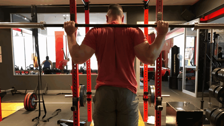 A professional powerlifting coach shows the narrow grip squat hand position.