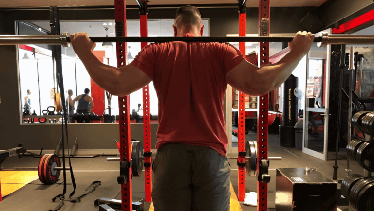 A strength coach shows the wide grip squat hand position.