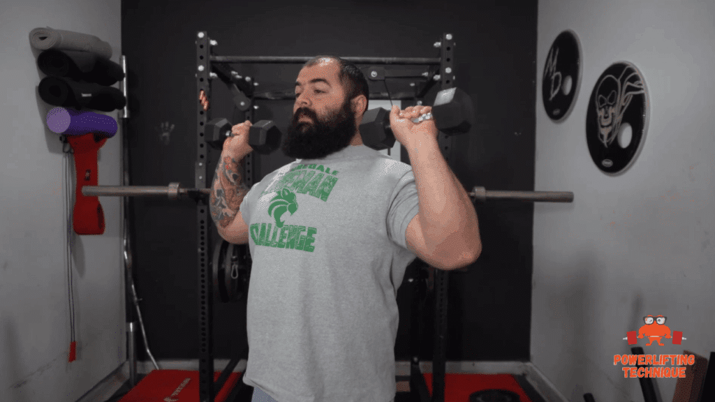 A strength training coach shows the bottom position of the dumbbell overhead press.
