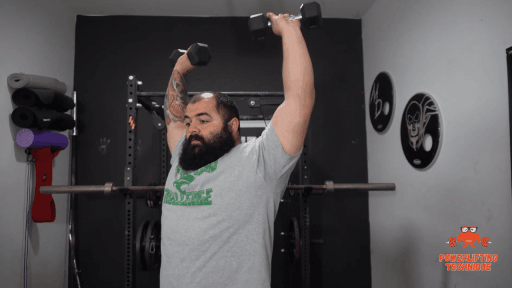 A strength training coach shows the top position of the dumbbell overhead press.