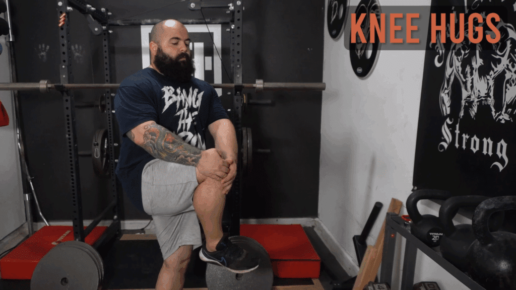 A strength coach shows how to do knee hugs.