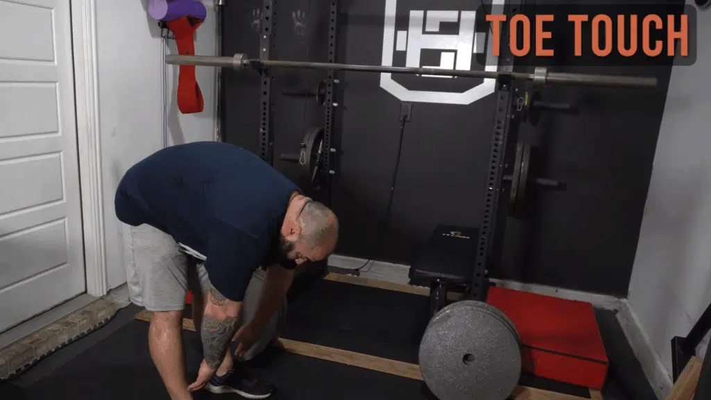 A strength coach shows how to do toe touches.