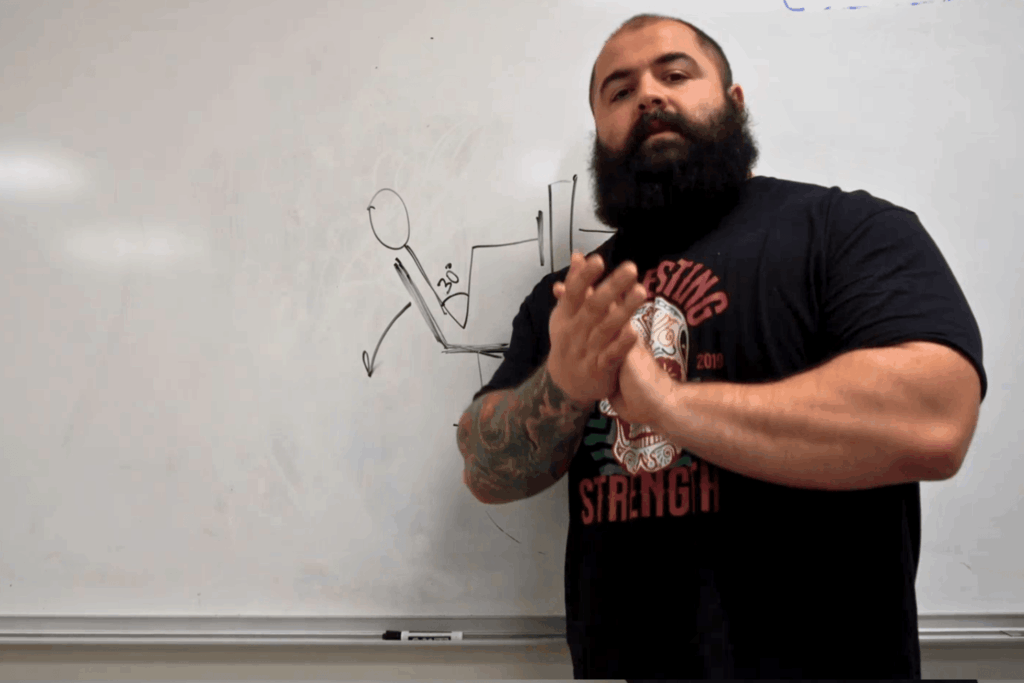 A professional strength coach stands in front of a whiteboard with a diagram of a person doing leg press at too small of an angle.